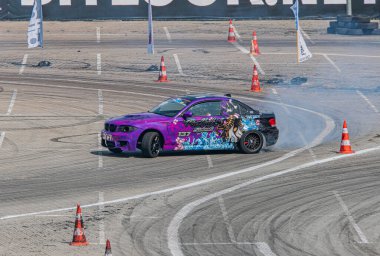 Mor BMW yarış pistinde canlı renkler, beyaz duman, turuncu koniler, gündüz aydınlatma, dinamik kompozisyon Kyiv, Ukrayna 06-15-2025