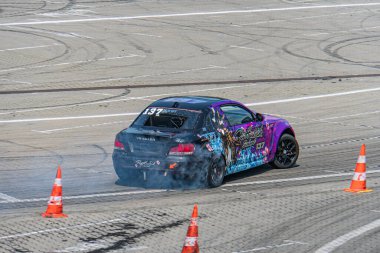 Pist üzerinde turuncu koni ile işaretlenmiş canlı mor BMW araba, açık gökyüzünün altında mavi, kırmızı elementler içeriyor ve Ukrayna, Kyiv, 06-15-2025 'ten kalma lastik izlerini gösteriyor.