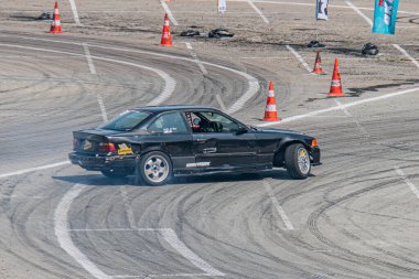 Açık hava yarış pisti, Kyiv Araba Sürükleme Festivali, BMW spor araba orta sürüklenme, siyah araç numara ve sponsorlu, turuncu koniler rehberlik için, parlak gün ışığı Kyiv, Ukrayna 06-15-2025