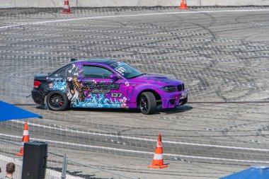 Mor BMW araba, mavi ejderha tasarımı, 23, canlı sokak yarışı sahnesi, turuncu güvenlik konileri ve çitlerle yarış pisti, kalabalık, öğleden sonra ya da ea Kyiv, Ukrayna 06-15-2025
