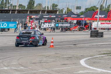 Kyiv 'de bir yarış tramvayı Kyiv, Ukrayna 06-15-2025' te akşam karanlığında düzenlenen Araba Sürükleme Festivali 'nde, BITCOIN ve BITROCKET de dahil olmak üzere sponsor logolarıyla süslenmiş siyah BMW araba.