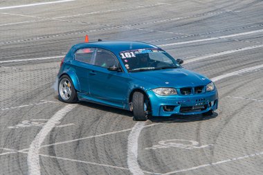 Aerodinamik özellikleri olan mavi bir BMW 'nin bulunduğu dinamik sürüklenme sahnesi asfalt pisti beyaz çizgiler ve kaldırımlarla işaretlenmiştir.