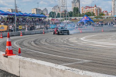 Kyiv Araba Sürükleme Festivali 'nde sürüklenen BMW arabası, parçalı bulutlu gökyüzü binalarının altında trafik konileri, lastik smo Kyiv, Ukrayna 06-15-2025
