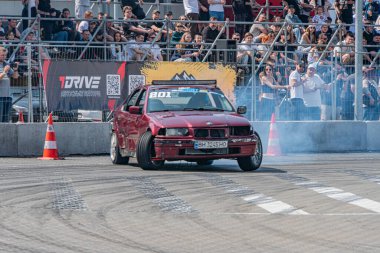 Kırmızı BMW arabası Kyiv Araba Sürükleme Festivali 'nde sürükleniyor. Lastiklerden dumanlar görünüyor. Seyircilerle birlikte asfalt yolda.