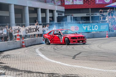 Kyiv Araba Sürükleme Festivali sırasında asfalt yolda sürüklenen kırmızı BMW arabası, bazıları renkli şemsiyeler altında parlak Kyiv, Ukrayna 06-15-2025