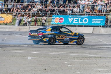 Sarı ve siyah çizgili mavi BMW arabası, Kyiv Araba Sürüklenme Festivali 'nde bir yarış pistinde sürükleniyor açık hava manzarasını aydınlatıyor, Natura Kyiv, Ukrayna 06-15-2025