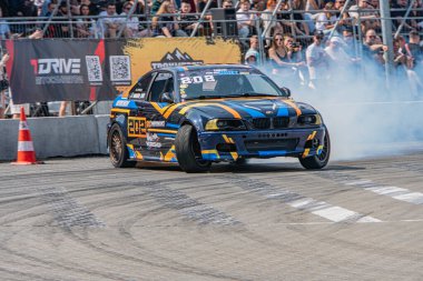 Kyiv Araba Sürükleme Festivali sırasında yarış pistinde sürüklenen mavi BMW arabası. Seyirciler arka plandan doğal ışıklandırma, yüksek perspektif, dinamik kompozisyon Kyiv, Ukrayna 06-15-2025 'i izliyor.