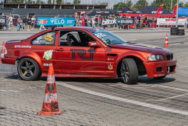 TRIUMPH işlemeli kırmızı BMW araba, turuncu ve beyaz koni işaretli bir pistte yarışıyor. Ukrayna, Kyiv, 06-15-2025 'ten izleyen gayri resmi izleyicilerin yakınındaki işaret levhasını başlat.