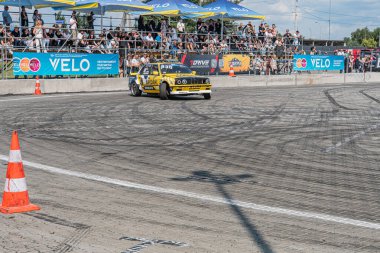 Kyiv Araba Sürükleme Festivali 'nde önde giden parlak sarı BMW koyu asfalt yolda dağılmış güvenlik tedbirleri, bulanık kalabalık, gün ışığı, gizli stil Kyiv, Ukrayna 06-15-2025