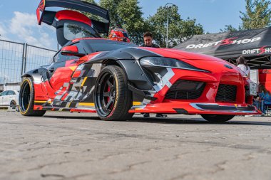 Açık hava araba etkinliği, canlı kırmızı Toyota Supra, aerodinamik tasarım, büyük lastikler, şemsiyeler, DRIFT Shop, parlak doğal ışık, yumuşak gölgeler, bulutlu veya dolaylı güneş ışığı Kyiv, Ukrayna 06-15-2025