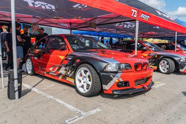 Bulutlu bir günde Kyiv Araba Sürüklenme Festivali 'nde kırmızı ve siyah BMW çadır altında daha az hareketli bir yarış arabası ya da Ca Kyiv, Ukrayna 06-15-2025' teki etkinlik personeli