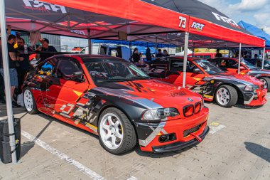 Kyiv 'de bir BMW' nin yer aldığı Araba Sürükleme Festivali, iki renkli araba çadırların altına park edilmiş bulanık bir kalabalığa karşı, doğal aydınlatma Kyiv, Ukrayna 06-15-2025