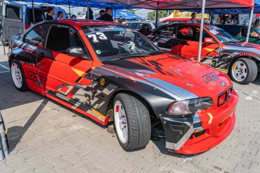 Tuğla yolda canlı kırmızı BMW yarış arabası, açılı gösterişli parlak tasarım, aerodinamik eğriler, zıt siyah çatı, yanında 79 ve 75 numara, büstl Kyiv, Ukrayna 06-15-2025