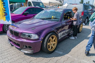 Mor, özelleştirilmiş yarış BMW 'si sokakta ya da kaldırımda sürüklenen araba festivalinde geniş vücut kiti, altın jantlar, ön tampon kanaryaları, arka spoiler Kyiv yakınlarında iki kişi, Ukrayna 06-15-2025