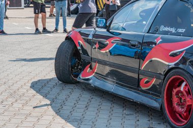 Alev grafikli siyah, modifiye edilmiş BMW arabası, halka açık bir etkinlikte tuğlalı bir alana park edilmiş ya da Ukrayna, 06-15-2025 Kyiv, Ukrayna 'daki aracı rasgele izleyen insanları bir araya getiriyor.