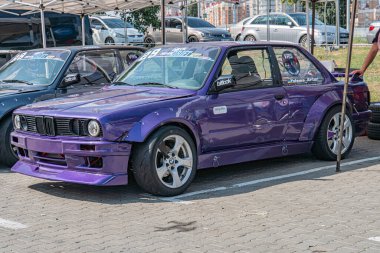 Kyiv Araba Sürükleme Festivali 'nde özel mor BMW arabası, yakındaki çadır ve araçlarla birlikte asfalta park edilmiş. Bireysel olarak sol tarafta kısmen görünmez. Doğal aydınlatma Kyiv, Ukrayna 06-15-2025