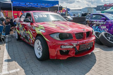 Kyiv Araba Sürükleme Festivali 'nde çarpan kırmızı BMW araba, alevlerle süslenmiş ve belirgin bir şekilde park edilmiş. Arka planda hareket halinde olan diğer benzersiz arabalar Kyiv, Ukrayna 06-15-2025