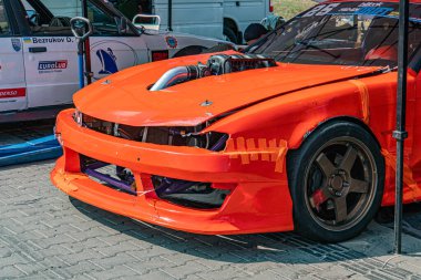 Yarış pistinde turuncu BMW yarış arabası, kaput yükseltilmiş, aerodinamik özellikler, bulutlu gün, yayılmış doğal ışık, gerçekçi belgesel tarzı Kyiv, Ukrayna 06-15-2025