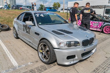 Kapalı araba fuarında modifiye edilmiş gri bir BMW, çıkartmalı pembe bir araba ve diğer özelleştirilmiş araçlar yer döşemesi, beyaz duvarlar, Kyiv, Ukrayna 06-15-2025 arabalarına hayran olan insanlar