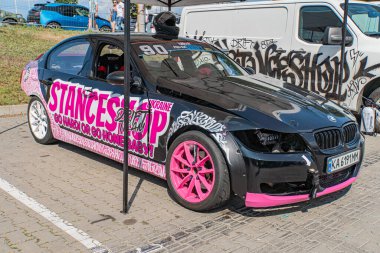 Kyiv Araba Sürükleme Festivali sırasında bir tuğla sokağa park edilmiş pembe beyaz üniformalı siyah BMW arabası Saintance ve pembe W Kyiv, Ukrayna 06-15-2025