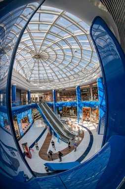 Modern alışveriş merkezi iç mimarisi, Blockbuster Alışveriş Merkezi Kyiv, mavi ve beyaz sütunlu büyük dairesel tavan penceresi, minimal gri döşeme, hareketli insan aktivitesi, Kyiv, Ukrayna 06-15-2025