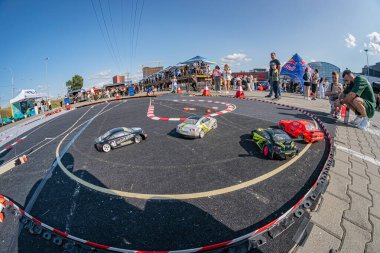 Kyiv 'de minyatür yarış pisti etkinliği, kırmızı ve beyaz çizgili bir pistte sürüklenen oyuncak arabalarla dağılmış izleyiciler bağlam, doğal gündüz aydınlatması, mavi gökyüzü Kyiv, Ukrayna 06-15-2025