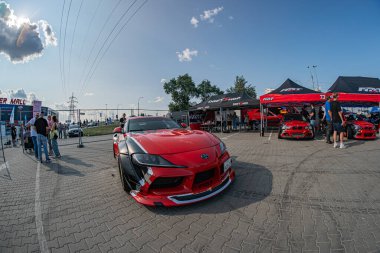 Kırmızı bir Toyota Supra arabasının bulunduğu açık hava otomotiv buluşması, aerodinamik eğrilerle hız ve performans sergiliyor arabanın etrafına dağılmış izleyiciler, i Kyiv çadırları, Ukrayna 06-15-2025