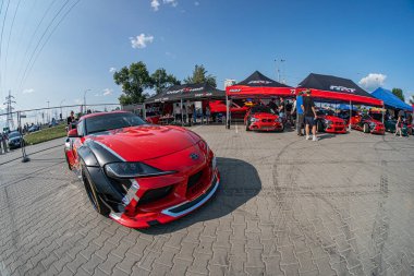 Kırmızı Toyota Supra arabası Kyiv Araba Sürükleme Festivali 'nde, üzerinde lastik izleri olan bir pistte park edilmiş parlak bir tasarım, arka planda gezinen çok sayıda insan, açılır kapanır çadırlar, Kyiv, Ukrayna 06-15-2025