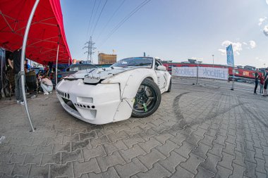 Beyaz açılı BMW araba çakıllı zeminde hasar görmüş, kırmızı bir tente çadırının yanında ve Kyiv Araba Sürükleme Festivali 'nde uzak seyirciler hatta aydınlatma, ca Kyiv, Ukrayna 06-15-2025