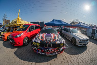 Dört eşsiz araç beyaz, turuncu, siyah SUV, Kyiv Clear gökyüzü, parlak güneş ışığı, asfalt yüzey, elektrik hattı Kyiv, Ukrayna 06-15-2025 'te çapraz olarak düzenlenmiş kırmızı yarış arabası.