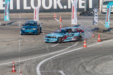 Mavi BMW arabası Kyiv Araba Festivali 'nde sürükleniyor, yarış pisti, turuncu trafik konileri, asfalt, mavi bayraklar, soldan sağa hareket, zıt renkler, yan görüş, parlak I Kyiv, Ukrayna 06-15-2025