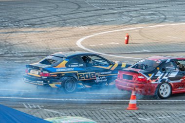 Alacakaranlıkta dinamik araba sürüklenme sahnesi, iki araba BMW, kırmızı röfleli mavi, yarış pistinde sarı çizgili beyaz yüksek hızlı dönüş sk Kyiv, Ukrayna 06-15-2025