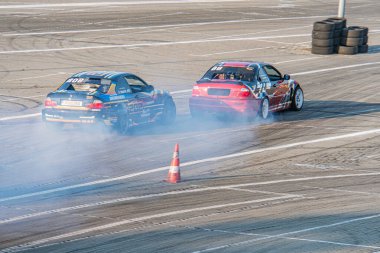 Kırmızı Kyiv Araba Sürükleme Festivali 'nde hızlı kovalamaca. Beton yarış pistinde mavi BMW' ler dönüyor. Sponsor logoları, kırmızı arabadan duman, çoklu Kyiv, Ukrayna 06-15-2025