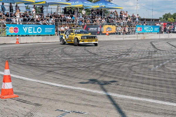 Kyiv Araba Sürükleme Festivali 'nde önde giden parlak sarı BMW koyu asfalt yolda dağılmış güvenlik tedbirleri, bulanık kalabalık, gün ışığı, gizli stil Kyiv, Ukrayna 06-15-2025