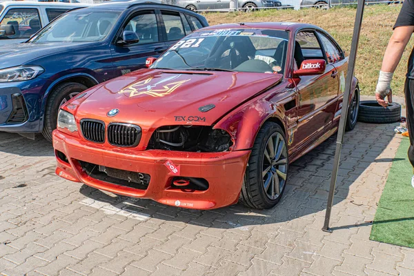 Kırmızı BMW yarış arabası motor sporları toplantısında ön tarafta hasar görmüş, çimenli arka planda siyah kaplı nesne, parlak gün ışığı, gizli görüntü tarzı Kyiv, Ukrayna 06-15-2025
