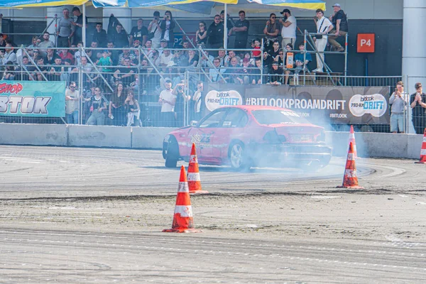 Güvenlik bariyerleri ve konileri olan yarış pistinde sürüklenen kırmızı bir araba, şemsiye altındaki izleyiciler ve çakıl gazı, dönen tekerlek Kyiv, Ukrayna 06-15-2025