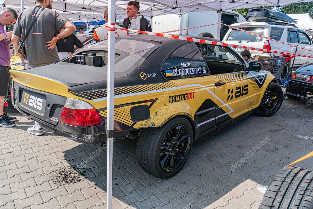 Yellow BMW car at a vibrant Kyiv Car Drifting Festival under a white tent Sleek and modern design with gold rims, number 56, and sponsor logos Bustling backgroun Kyiv, Ukraine 06-15-2025