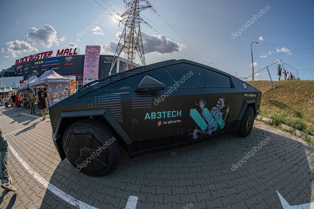 Futuristic black Cybertruck with vibrant graphics parked on a brick pavement at an outdoor event, possibly a race track Other high-performance vehicles in backgroun Kyiv, Ukraine 06-15-2025