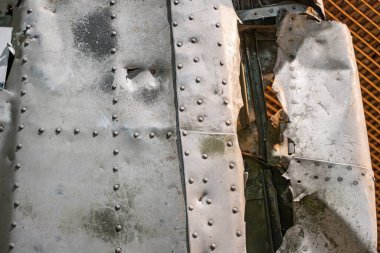 Düzensiz yüzeyi ve görünür çukurları olan hasarlı bir metal uçak parçasının yakın görüntüsü gölgeler oluşturur. Doku ve detaylara odaklanan gerçekçi bir metin mevcut değildir.