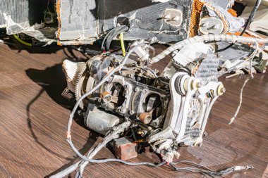 Rus İHA parçalarının endüstriyel bir ortamda dağılmış halinin yakın görüntüsü. Keskin bir şekilde metalik merkezi bir parçaya odaklanıyor. Elektronik bileşenler ile çevrelenmiş daha küçük elementler muhtemelen b