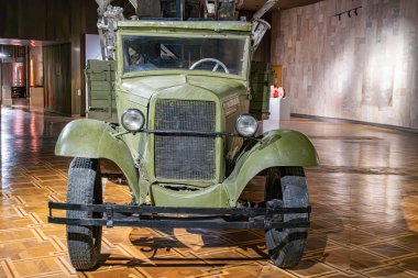 Kapalı bir müze ayarında eski bir askeri kamyonet off-road lastikleri, soluk yeşil renk, paslı yapay ışıklandırma mevcut değil.
