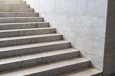 Modern, minimalist mermer merdiven doğal ışık altında mimari özelliklerle kısmen gizlenmiş. a