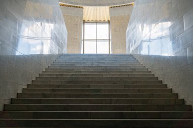Büyük mermer mermer merdiven, üst kattaki pencerelerden yansıyan doğal ışık ile aydınlatılmış, yansıtıcı taş duvarlar, metin yok, düz stil, tam yükseklik yakalama ve davet