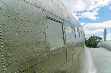 Eski model askeri uçak, ağırlıklı olarak yeşil, açık havada park halinde, düz kanatlar, kapı ve pencereli birden fazla kompartıman, kuyruk yüzgeçleri, uçak gövdesi işaretleri, öğle vakti aydınlatma, açık gökyüzü, birkaç dağınık