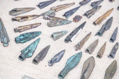 Arkaplana yayılmış ok başları, çeşitli boyutlarda ve sivri şekilli ağırlıklı taş ya da sert malzeme tonlarında kahverengi, gri, siyah renkte ve üzeri yazılı değil, hatta kalın perspektifli bile değil.