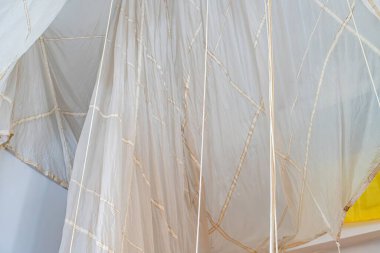 Beyaz, buruşuk yelkenli, bambu destekli kaburgalı, muhtemelen geleneksel bir tekne ya da sanat eseri, yelken boyunca güneş ışığı akışının oluşturduğu bir direkten asılı.