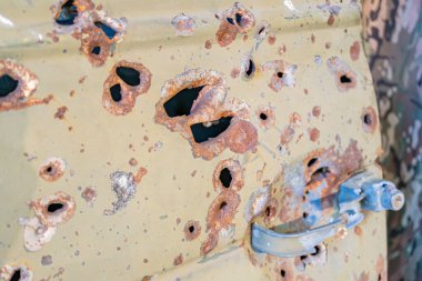 Çok sayıda kurşun deliği olan yıpranmış, hasarlı bir araca yakın çekim. Kahverengi ve siyah renk şeması. Bağlam sağlanamadı.