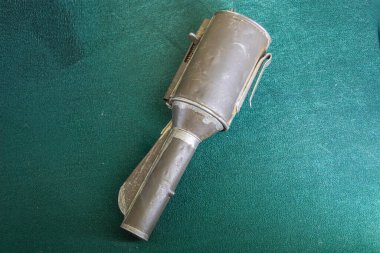 Yıllanmış, silindirik metal bir fener. Sapı ve aşınma izleri var. Tanımlanamayan bir arka plana yerleştirilmiş.