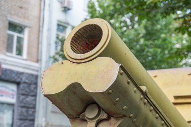 Tank ön ucu, büyük silah namlusu, kentsel çevre, yıpranmış, paslı, metalik yüzey, silindirik şekil, alevli ağız, koyu renk, doğal aydınlatma, sol taraf gölgesi, mevcut insan yok