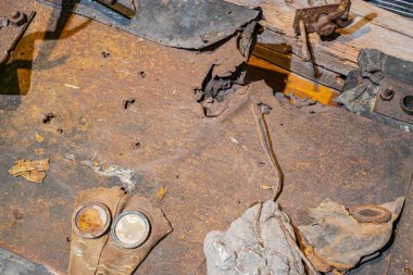 Paslı metal zemin üzerindeki iç mekan enkaz, inşaat malzemeleri ve küçük metalik bir nesne ile dolu.